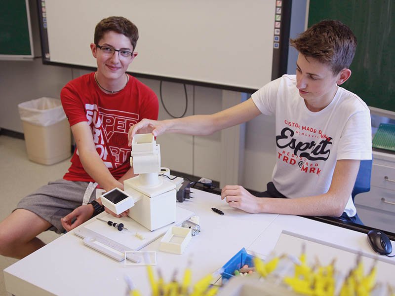 Schüler mit Handschuh und einer bionischen Hand auf dem Tisch