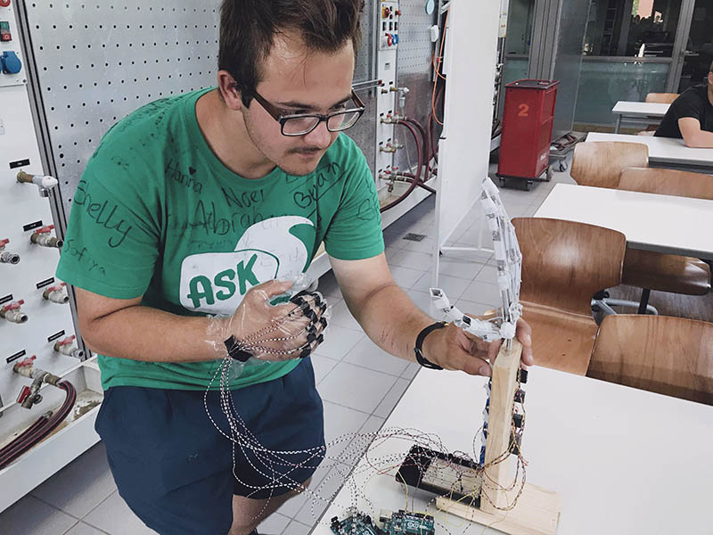Schüler mit Projektarbeit, er trägt einene Handschuh und auf dem Tisch steht die bionische Hand