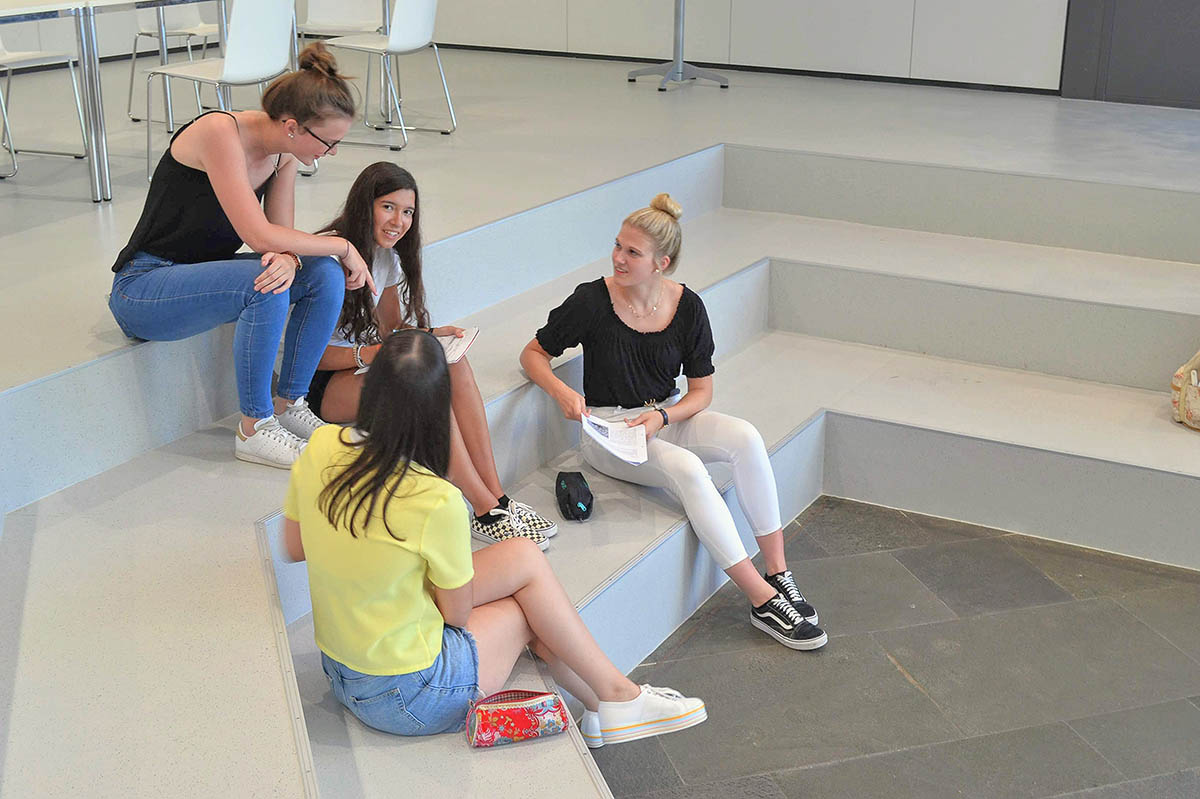 Schulcampus Schülerinnen unterhalten sich, sitzen im Schulcampus auf Treppe